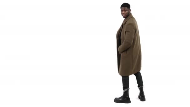 Elegante uomo africano con cappotto invernale e girando verso la fotocamera isolato su sfondo bianco copiare spazio — Video Stock
