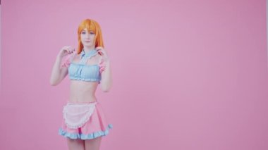 20 'li yaşlarındaki Avrupalı garson kız kızıl saçlarıyla flört ediyor. Pembe arka planda fotokopi alanı yaratıyor.