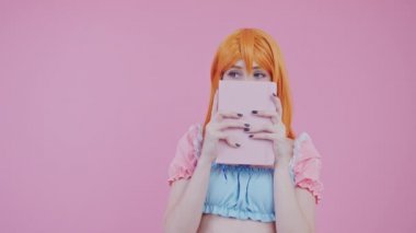 Kızıl saçlı Avrupalı ürkek genç yüzünü pembe günlük pembe arka plan stüdyo fotoğrafının arkasına gizliyor.