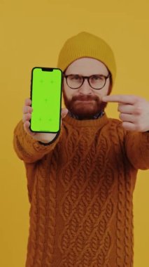 Kafkasyalı orta yaşlı bir adamın yeşil ekranlı akıllı telefonunu işaret edişinin dikey çekimi.