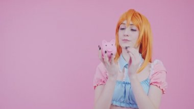 Neşeli Avrupalı 20 'li yaşlarda bir kadın kumbarasında çok parası olan pembe arka plan çekimleri yapıyor.