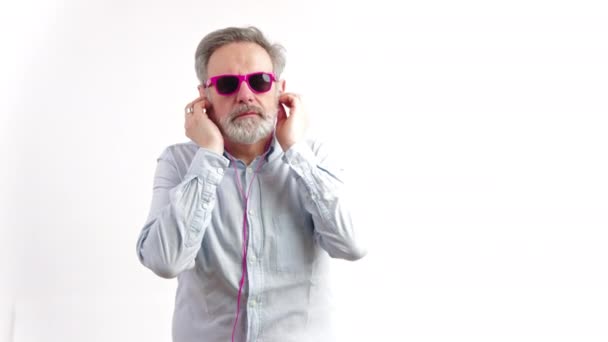 Кавказький старший носить рожеві сонцезахисні окуляри та навушники - танцюючі ізольовані на білому фоні. — стокове відео