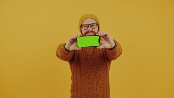 Hombre barbudo caucásico sosteniendo el teléfono inteligente horizontalmente con pantalla verde y sonriendo a la cámara — Vídeos de Stock