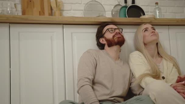 Portré Y-generációs kaukázusi pár ül a konyhapadlón, kötés, összebújás, és gondolkodás — Stock videók