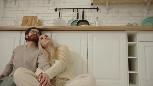 Piękny kaukaski para siedzi na podłodze w nowoczesnej kuchni i patrząc w górę, myśląc o przyszłości — Wideo stockowe
