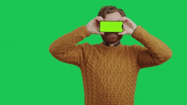 Кавказский молодой предприниматель держит макет зеленого экрана смартфона перед глазами средний студия снята на зеленом фоне — стоковое видео