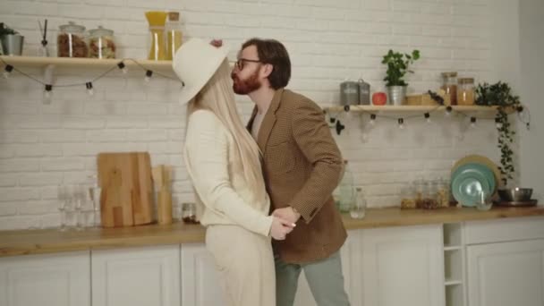 Fiatal európai férj táncol gyönyörű hosszú hajú feleségével a konyhában, az évfordulójukat ünnepli — Stock videók
