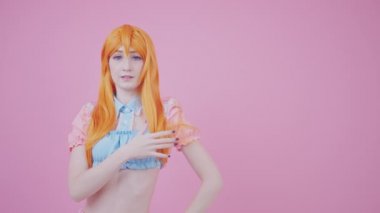 20 'li yaşlarında, kızıl saçlı, parlak, sağlıklı saçlarıyla poz veren, pembe arka plan, yakın çekim stüdyo fotoğrafı.