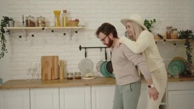Avrupalı orta yaşlı sakallı bir adam nişanlısını modern, parlak mutfaklarında sırtında taşıyarak eğleniyor.