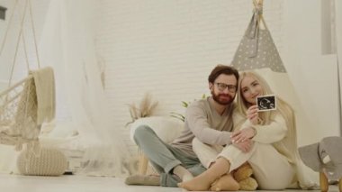 Yakında beyaz anne baba olacak kişiler yerde oturuyor ve kameraya hamileliğin ultrason taramasını gösteriyorlar.