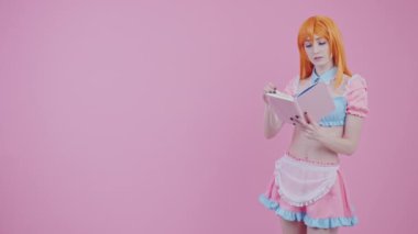Genç, kızıl saçlı, beyaz kadın, 20 'li yaşlarda. Pembe bir kitaptan, orta boy bir fotoğraf stüdyosundan ilginç bir şekilde okuyor.