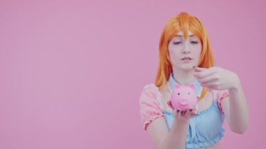Beyaz tenli şirin bir genç para kutusuna bozuk para atıyor. Pembe arka plan orta stüdyo fotoğrafı.
