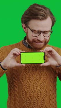Dikey çekim genç beyaz girişimci elinde sahte yeşil ekran akıllı telefonuyla kameraya gülümsüyor.
