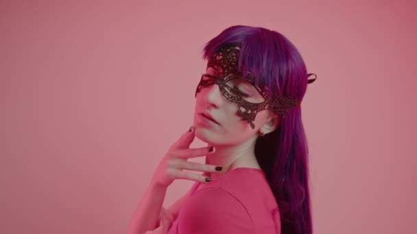 Mysterious European Masked Woman in her 20s slowly touches her chin and thinks medium close-up shot pink background — Stock Video