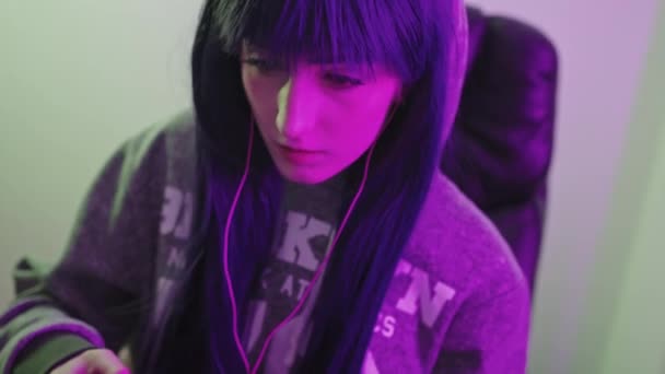 Joven chica de cabello oscuro en una sudadera con capucha utiliza sus habilidades gamepad para ganar un juego de tiro de cerca medio — Vídeo de stock