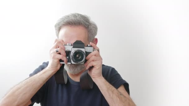 Im Alter gut aussehender Fotograf beim Fotografieren mit Filmkamera - weißer Hintergrund — Stockvideo