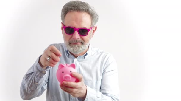 Hombre mayor en gafas de sol de color rosa que sostiene la alcancía - ahorros y feliz concepto de jubilación — Vídeo de stock