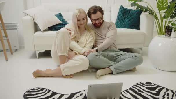 Europejska blondynka o długich włosach piękna siedzi na podłodze ze swoim kochającym partnerem i ogląda filmy na swoim laptopie — Wideo stockowe