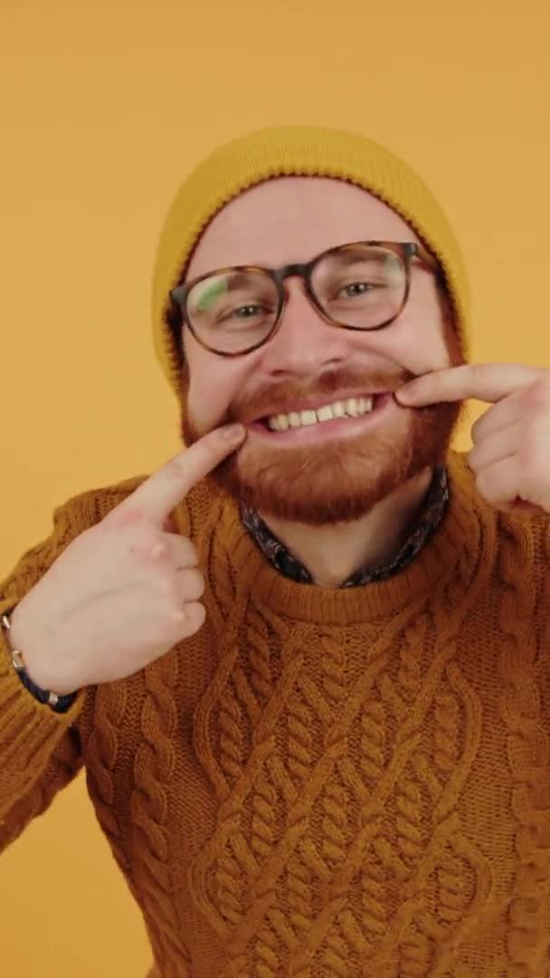 Χαρούμενος φιλικός καυκάσιος μεσήλικας γενειοφόρος άντρας αγγίζει το πρόσωπό του και δείχνει τα λευκά υγιή δόντια του κάθετα στούντιο πυροβόλησε κίτρινο φόντο — Αρχείο Βίντεο