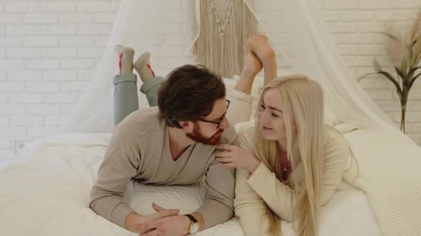 Ung entreprenör och hans vackra affärskvinna flickvän lägga sig på sin säng, vara lekfull, leende, och titta på kameran — Stockvideo