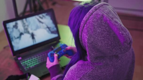 Jong brunette in een hoodie maakt gebruik van gamepad en moedigt aan om te spelen met haar medium close-up shot — Stockvideo
