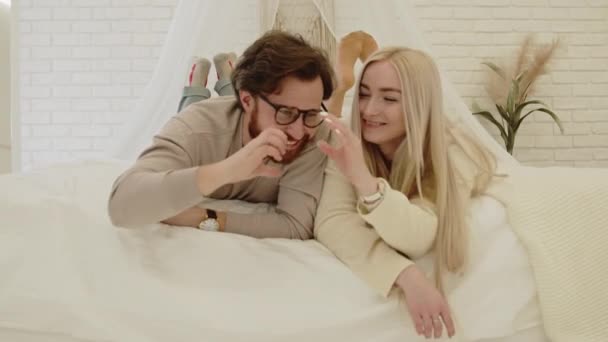 Söta kaukasiska par tittar på varandra bildar hjärtform med sina handflator när de ligger på sängen — Stockvideo