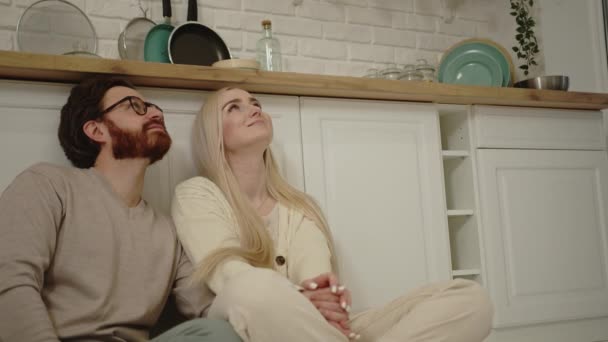 Przytulne kaukaskie para siedzi na podłodze w nowoczesnej kuchni i patrząc w górę, myśląc o przyszłości — Wideo stockowe