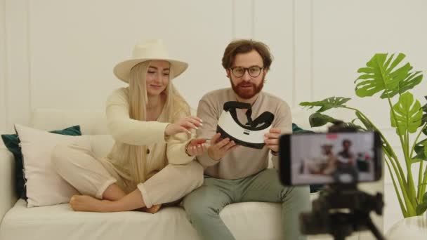 Fröhliche europäische Influencer erstellen ein neues Video, während sie auf einer weißen Couch in ihrer modernen Wohnung sitzen — Stockvideo