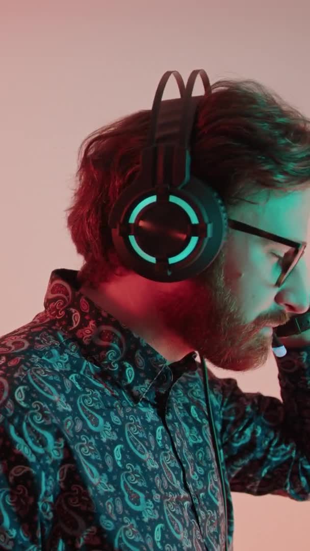 Vertical tiro joven caucásico elegante hombre en gafas con auriculares escuchando música y bailando estudio tiro pastel rosa fondo — Vídeos de Stock