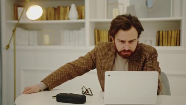 Alvorlig og bekymret kaukasisk skægget iværksætter ser på skærmen på sin bærbare computer, mens hans smukke kone kommer til ham for at vise sin støtte – Stock-video