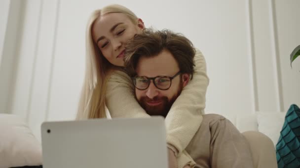 Sevecen beyaz bir çift oturma odasında oturuyor ve gümüş bir dizüstü bilgisayar kullanarak internette geziniyorlar. — Stok video