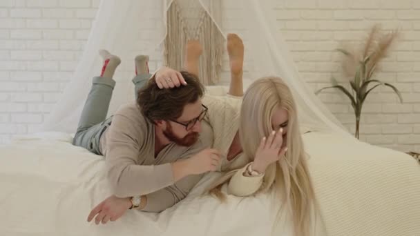 Älskade kaukasiska unga par ligger tillsammans i sängen, kramas och skrattar — Stockvideo
