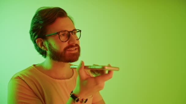 Schöner bärtiger Hipster-Millennial-Mann im gelben T-Shirt, der in seinem Smartphone-Studio per Lautsprecher mit jemandem spricht — Stockvideo