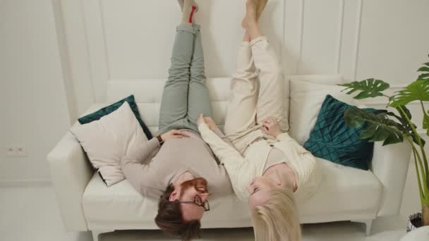 Šťastný pár v jejich 30s ležící na pohovce v jejich zbrusu novém bytě zvedání nohy nahoru a vtipkování — Stock video