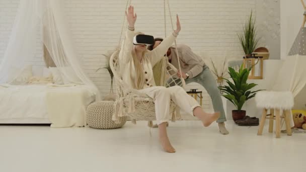 Молодой кавказский предприниматель показывает своей блондинке-невесте технологию очков VR в их современной квартире — стоковое видео