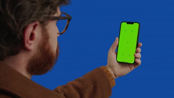 Kavkazský muž středního věku s vousy pomocí chytrého telefonu se zelenou obrazovkou a gesty přes modrou obrazovku — Stock video