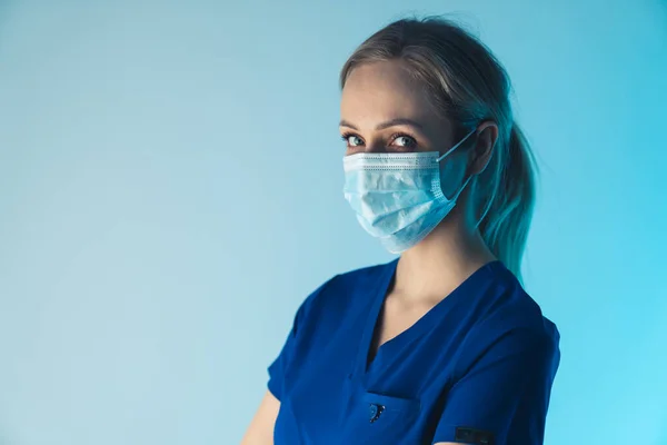 Ernsthafte Gesundheitsarbeiterin blickt in die Kamera und trägt eine chirurgische Maske, um die Ausbreitung von Bakterien und Viren zu verhindern. — Stockfoto