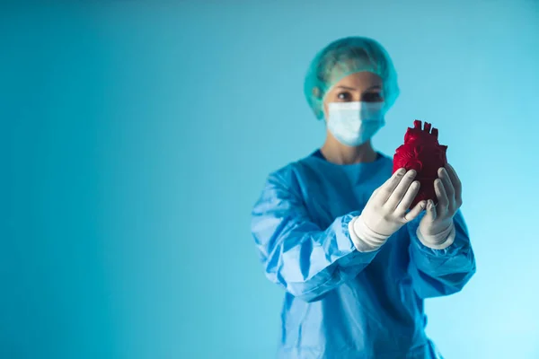 Médico mascarado e totalmente preparado segurando coração vermelho artificial. Conceito de saúde. — Fotografia de Stock
