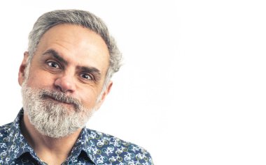 Beyaz saçlı, orta yaşlı, beyaz bir adam kameraya komik bir yüz ifadesi takınıyor.