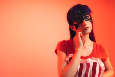 Yakından çekilen, büyük gözlü, maske takmış Avrupalı kız arkadaş kameranın pembe arka planına yumuşak ve şehvetli bir şekilde bakıyor.