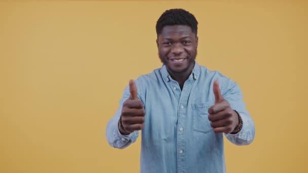 Alegre Feliz Afro Americano Sonriendo a la cámara aislado sobre fondo naranja mostrando los pulgares hacia arriba gesto — Vídeos de Stock