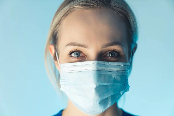 Enfermeira caucasiana confiante usando máscara profissional, educa sobre segurança. close up studio shot, fundo azul. — Fotografia de Stock