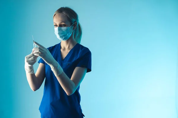 Gemaskerde blanke dokter draagt een uniform met een injectie in haar handen. Gezondheidszorg en ziektepreventie. — Stockfoto