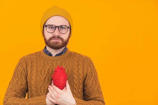 Мужчина около 30 лет держит реалистичное пластиковое сердце близко к телу, делая серьезное лицо — стоковое фото