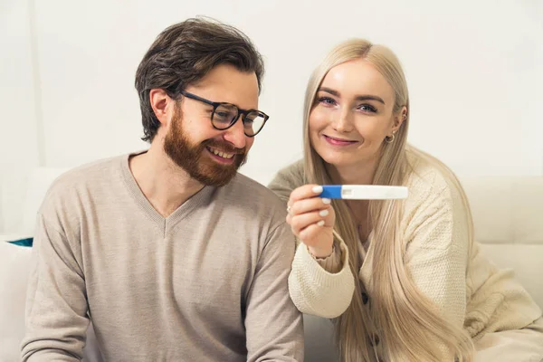 Jovem mulher grávida casal caucasiano animado mostrando um teste de gravidez positivo para o retrato da câmera — Fotografia de Stock