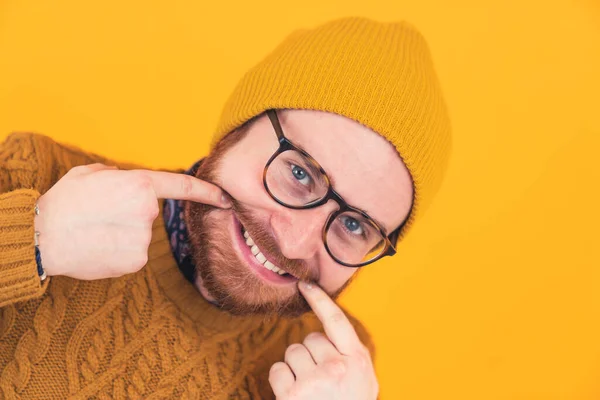 Крупный план веселый молодой бородатый кавказский мужчина улыбается в очках и шляпе, мужчина трогает края рта, показывая зубы оранжевый фон изолированная студия снимка — стоковое фото