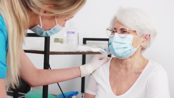 Indoor portret van mooie oudere vrouw in beschermende gezichtsmasker praten met haar verpleegkundige tijdens gezondheidscontrole. — Stockvideo