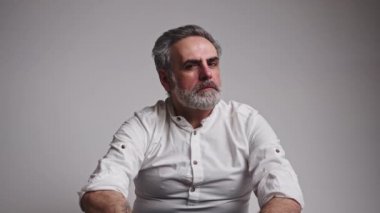 Yaşlı bir adam ellerini saçlarında gezdiriyor, gri arka plan, orta derecede yakın çekim.