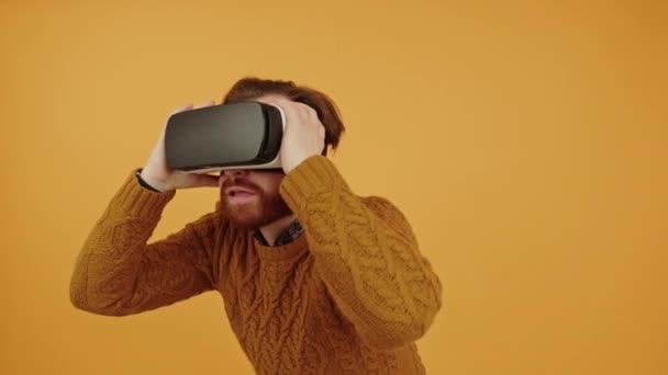 Překvapený mladý běloch hraje videohry pomocí vr brýle, dotkne se pak oběma rukama virtuální realita koncept kopírovat prostor oranžové pozadí izolované — Stock video