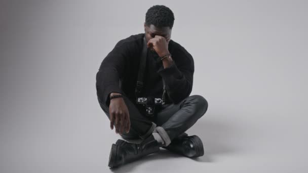 Zwarte man kijkt zichtbaar verdrietig en waarschijnlijk huilen vanwege de problemen in zijn leven zitten op de vloer, grijze achtergrond — Stockvideo